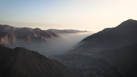 Una-Foto-De-Un-Dron-De-Un-Valle-Brumoso-Con-Montañas-A-Un-Lado-Durante-La-Puesta-De-Sol-En-Perú