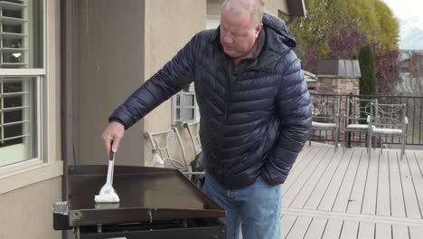 Mature-man-wiping-down-his-flat-top-griddle-with-oil-after-a-cook