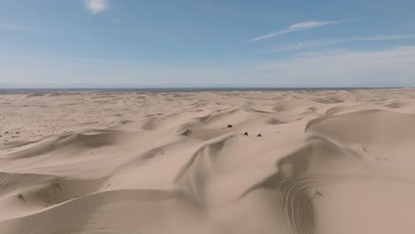 Drone-Shot-in-Sunny-Sand-Dunes,-ATV-Dune-Buggies-Driving-Through-Peaks
