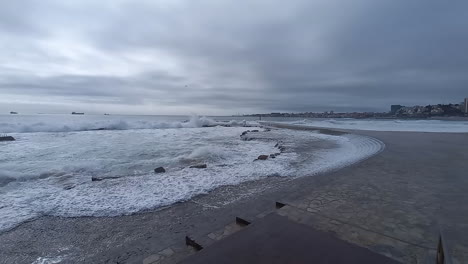 Very-rough-sea-causes-the-waves-to-pass-over-the-sauce-and-reach-the-pedestrian-zone,-gray-sky-with-rain