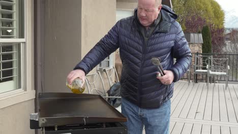Older-man-pours-oil-on-a-hot-flat-top-griddle-to-season-after-cooking