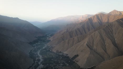 Drone-shot-of-a-green-valley-with-a-river-surrounded-by-mountains-during-sunset-in-Peru