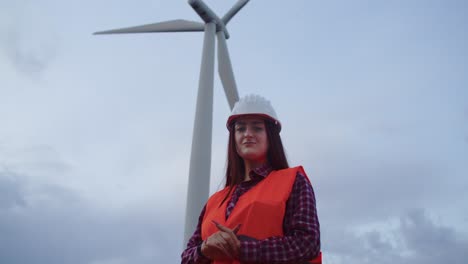 Woman-engineer-technician-smiles-looking-at-camera-with-wind-turbine-behind