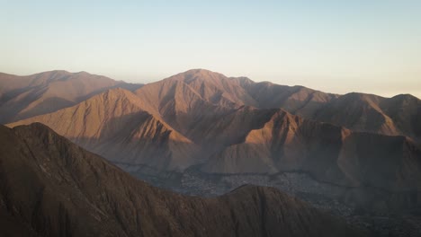 Eine-Drohne,-Die-Während-Des-Sonnenuntergangs-Von-Bergen-Neben-Einer-Stadt-In-Peru-Aufgenommen-Wurde