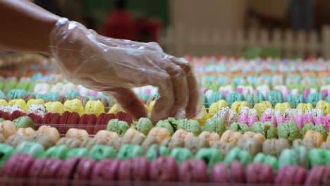 Vendor's-Hand-In-Disposable-Plastic-Glove-Arranging-Colorful-Macarons-In-Rows