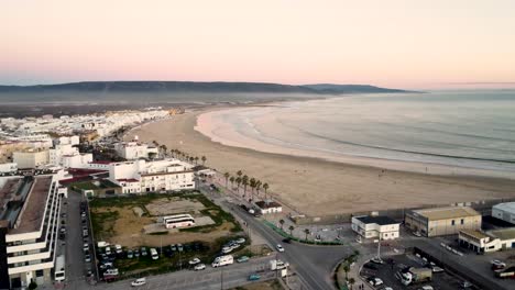 Aerial-flyover-over-a-seafront-town-with-a-stunning-tropical-beach-during-sunset