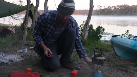 A-man-boils-water-on-a-gas-stove-at-a-remote-camp-on-an-Australian-lake