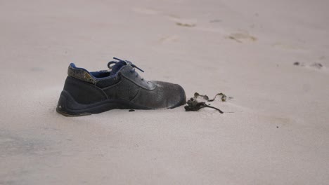 Old-shoe-on-the-beach,-trash-and-waste-litter-on-an-empty-Baltic-sea-white-sand-beach,-environmental-pollution-problem,-overcast-day,-medium-closeup-shot