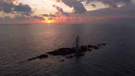 Sensational-aerial-view-of-sunset-with-Lighthouse-on-offshore-rocks,-dolly-out