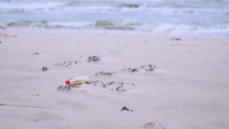 Small-glass-bottle-on-the-beach,-trash-and-waste-litter-on-an-empty-Baltic-sea-white-sand-beach,-environmental-pollution-problem,-overcast-day,-medium-shot