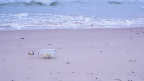 Empty-glass-bottle-on-the-beach,-trash-and-waste-litter-on-an-empty-and-clean-Baltic-sea-white-sand-beach,-environmental-pollution-problem,-overcast-day,-medium-shot