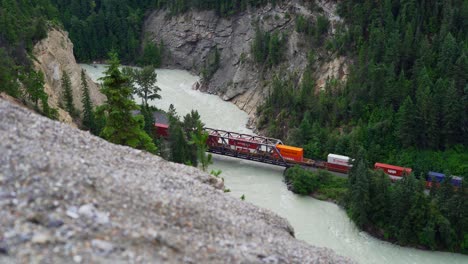 Cargo-freight-train-travelling-across-a-river-in-the-beautiful-landscape-of-Golden-British-Colombia-Canada