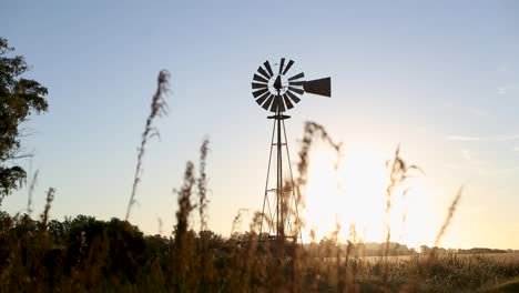 Focus-shift-from-grass-to-old-windmill-water-pump-on-field-at-sunset