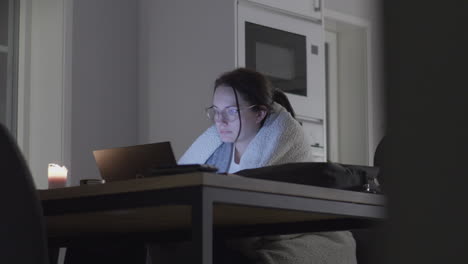 Woman-in-the-kitchen-wrapped-in-a-blanket-studying-on-the-computer