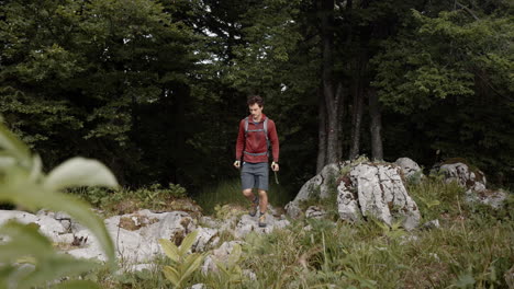 Man-with-the-backpack-walking-with-the-hiking-poles-out-of-the-forest-on-big-rocks-to-reach-a-certain-destination