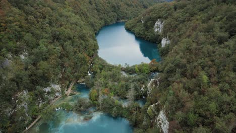 Turquoise-river-in-wooded-rocky-canyon-of-Plitvice,-Croatia,-flyover