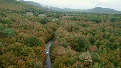 Car-driving-on-road-winding-through-autumn-forest-in-Croatia,-drone