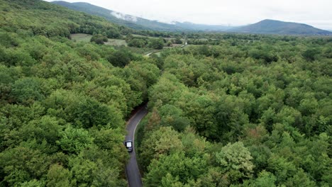 Car-driving-through-green-forest-on-asphalt-road-in-Croatia,-drone