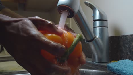 Man-open-faucet-and-clean-yellow-pepper-in-sink-with-high-pressure-water---medium-shot