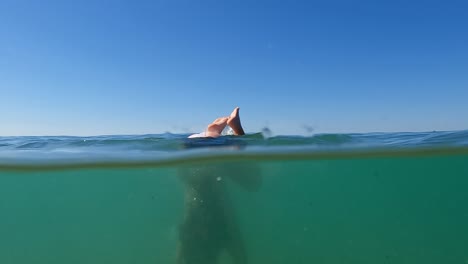 Half-underwater-scene-of-young-redhead-girl-doing-handstand-in-seawater-with-horizon-in-background