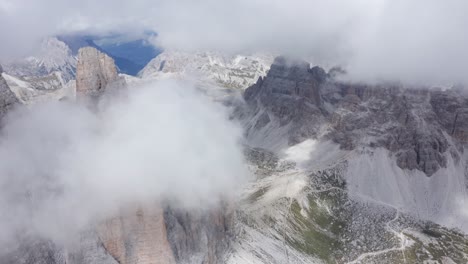 Aerial-top-down-shot-of-flying-clouds-covering-Mountain-peaks-of-Dolomites-in-sunlight---rocky-Hiker-path-in-the-valley-of-South-Tyrol