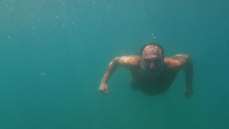 Underwater-scene-of-adult-man-in-apnea-swimming-toward-camera-while-smiling