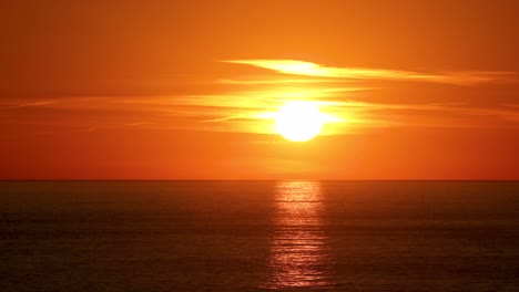 Beautiful-sun-behind-dramatic-orange-clouds-in-sunset-sky-over-ocean