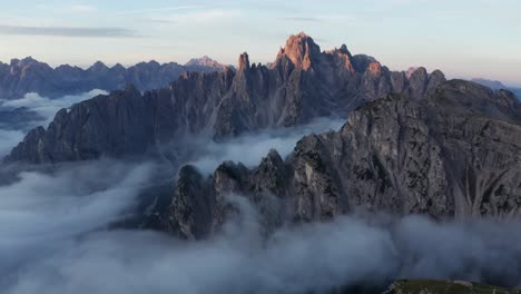 Mysterious-sunrise-drone-shot-of-clouds-covering-Cadini-Di-Misurina-Mountain-range-in-the-Dolomites,-Italy