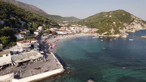 Aerial-View-Of-Parga-Beach-Lined-With-Umbrellas-On-Sunny-Day-With-Boats-Moored-In-The-Ionian-Sea