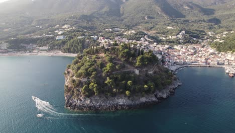 Aerial-View-Of-Venetian-Castle-Of-Parga-Town-In-Epirus-With-Speedboat-Going-Past-In-Waters-Below