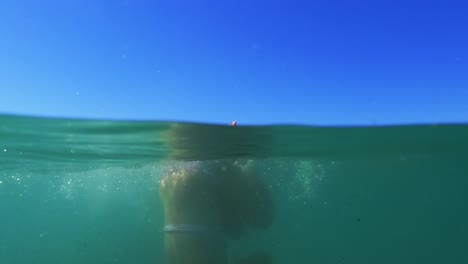 Half-underwater-scene-of-young-redhead-girl-rolling-back-in-sea-water-with-horizon-in-background