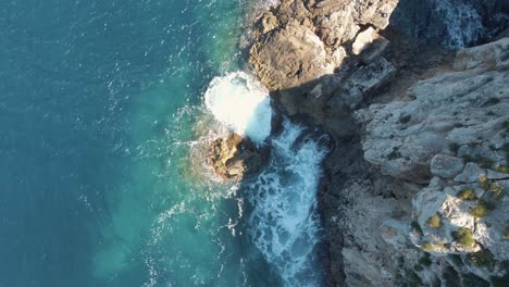 Aerial-Looking-Down-At-Waves-Crashing-Onto-Rocks-At-Cala-Llonga,-Ibiza