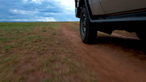 Filmación-De-La-Rueda-Delantera-Y-La-Parte-Delantera-De-Un-Jeep-En-Movimiento-Conduciendo-Por-Una-Pista-A-Través-De-La-Sabana-En-áfrica