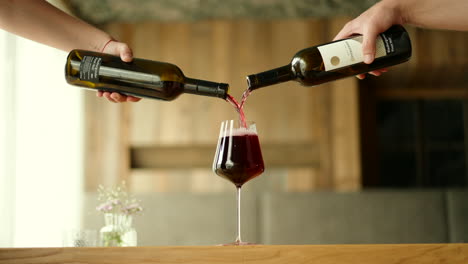 Rotwein-Wird-Aus-Zwei-Flaschen-In-Ein-Glas-Gegossen
