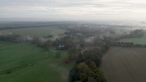 Flying-over-an-Autumn-coloured-tree-line-towards-a-small-village-in-the-fog