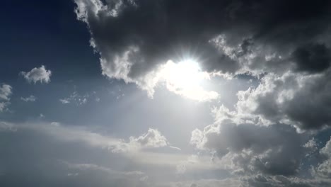 Bright-sun-peeking-through-large-gray-clouds-in-the-blue-sky