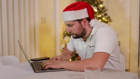 caucasian-entrepreneur-businessman-working-from-home-with-a-Santa-hat-during-xmas-holiday-typing-on-a-laptop-with-a-glass-of-whiskey-near-a-Christmas-tree