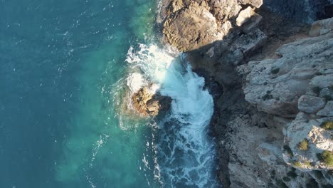 Aerial-shot-of-turquoise-sea-water-hitting-rock-at-Cala-Llonga-Mexican-Island