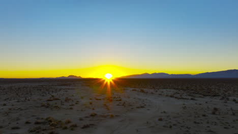 Sunset-with-the-golden-fiery-orb-of-the-sun-just-above-the-mountainous-horizon-in-the-Mojave-Desert---push-forward