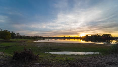 Majestic-sunset-reflects-on-lake-water-in-vibrant-rural-landscape,-wide-angle-lens