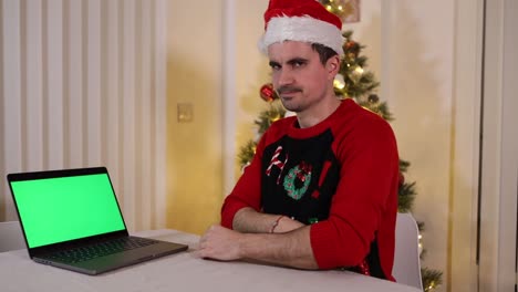 caucasian-male-looking-at-the-green-screen-laptop-with-disappointment-and-disbelieve-during-Christmas-holiday-meeting-at-his-home-office-with-a-Xmas-tree-in-the-background