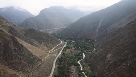 Tilting-drone-shot-of-a-road-next-to-a-river-in-between-mountains-in-the-highlands-of-Peru