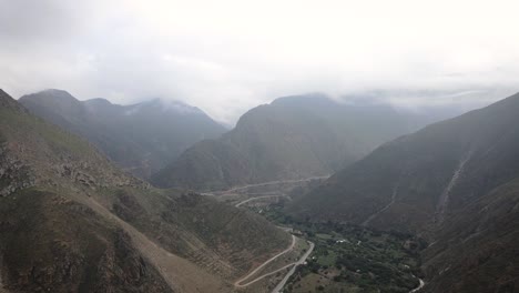 Circling-misty-drone-shot-of-a-road-in-between-green-and-rocky-mountains-in-the-highlands-of-Peru