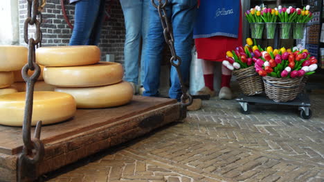 Dutch-Gouda-Cheese-And-Colorful-Tulips-Displayed-At-Goudse-Waag-With-Cropped-Portrait-Of-People-Buying,-Famous-Gouda-Market-In-The-Netherlands