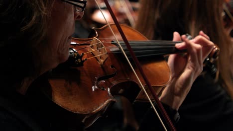 Extreme-close-up-slow-motion-of-a-talented-violin-player-performing-with-a-wooden-violin-with-orchestra-during-a-concert-with-classical-music-to-mozart-with-view-of-other-violin-players