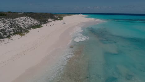 Young-Couple-Walk-on-White-Sand-Beach-from-behind,-aerial-shot-dolly-in-stunning-caribbean-background