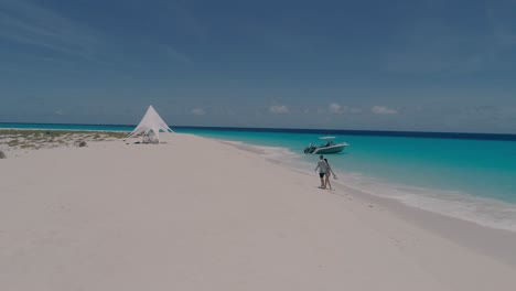 Couple-Walking-barefoot-on-Tropical-white-sand-Beach-Towards-Camping-Tent,-drone-shot