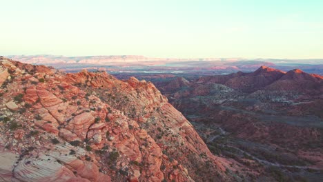 Atemberaubende-Luftaufnahme-Von-Roten-Und-Orangefarbenen-Bergen-Und-Einem-Grünen-Tal-In-Yant-Flats,-Utah-Bei-Sonnenuntergang-In-Der-Nähe-Von-St