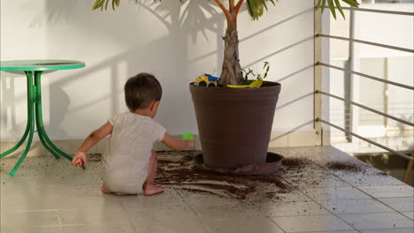 Young-naughty-latin-baby-boy-dropping-soil-on-the-floor-at-this-home-from-a-plant-pot-on-a-summer-afternoon