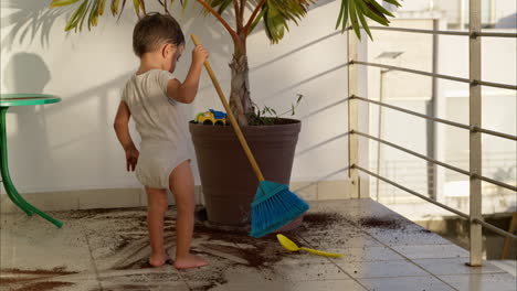 Young-latin-toddler-sweeping-dirt-from-the-floor-after-soiling-it-with-dirt-from-a-plant-pot